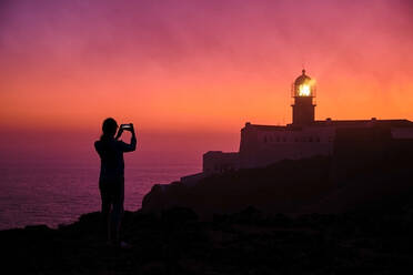 Portugal, Algarve, Silhouette einer Person, die Smartphone-Fotos von Cape Saint Vincent Leuchtturm in der Morgendämmerung - MRF02164