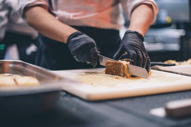 Koch bei der Arbeit, der einen Kuchen in einer Restaurantküche anschneidet - CJMF00095