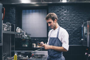 Koch mit Smartphone in der Küche eines Restaurants - CJMF00096