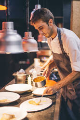 Chef serving food on plates in the kitchen of a restaurant - CJMF00098