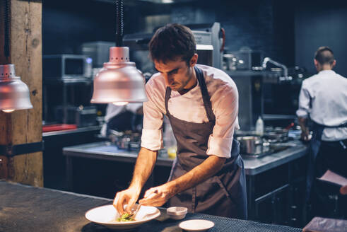 Koch serviert Essen auf einem Teller in der Küche eines Restaurants - CJMF00106