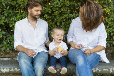 Parents with happy little daughter sitting on a bench - MGIF00764