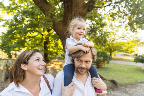 Happy family in a park with father carrying little daughter on his shoulders stock photo