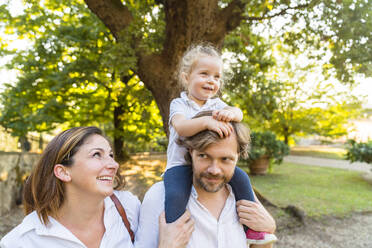 Glückliche Familie in einem Park, der Vater trägt seine kleine Tochter auf den Schultern - MGIF00781