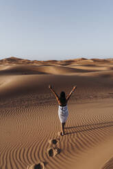 Rückansicht einer jungen Frau beim Wandern in der Wüste, Merzouga, Marokko - DAMF00126