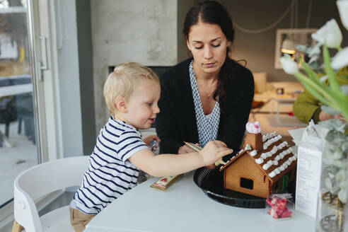 Mutter mit Sohn beim Verzieren eines Lebkuchenhauses - JOHF02259