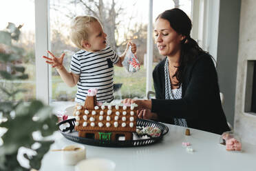 Mutter mit Sohn beim Verzieren eines Lebkuchenhauses - JOHF02261