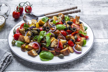Panzanella, italienischer Brotsalat mit geröstetem Ciabatta, Tomaten, Oliven, roten Zwiebeln, Kapernäpfeln und Basilikum auf Teller - SARF04373