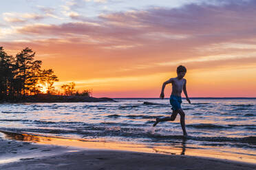 Junge läuft am Strand bei Sonnenuntergang - JOHF02363