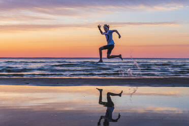 Boy jumping on beach at sunset - JOHF02365