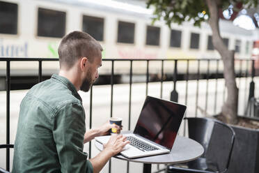 Mann mit Laptop in einem Straßencafé - JOHF02523