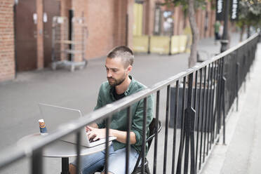 Man using laptop in outdoor cafe - JOHF02524