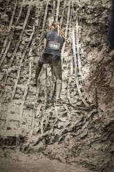 Woman climbing muddy cliff - JOHF02532