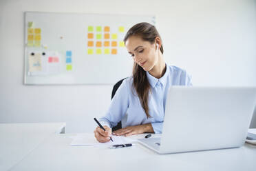 Young businesswoman preparing business documents while working with laptop in office - BSZF01494