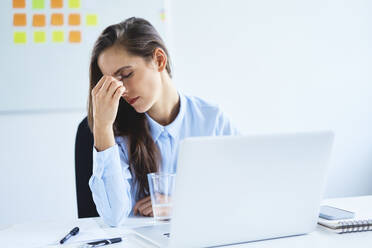Young woman sitting in office with headache - BSZF01497
