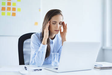 Young businesswoman holding head suffering from headache in office - BSZF01498