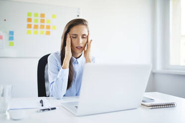 Young businesswoman sitting in office suffering from headache - BSZF01499