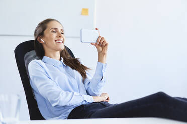 Young businesswoman sitting in office during phone video call - BSZF01501