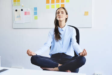 Junge Geschäftsfrau sitzt auf einem Bürostuhl und meditiert - BSZF01503