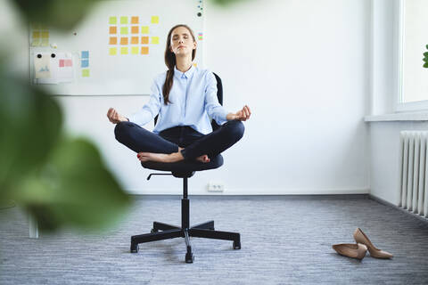 Gelassene junge Frau, die auf einem Bürostuhl sitzend meditiert, lizenzfreies Stockfoto