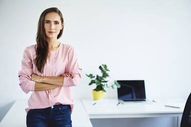 Portrait of confident young businesswoman leaning against desk in office - BSZF01511
