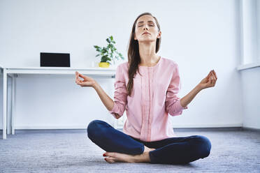 Young woman meditating on floor in office - BSZF01517