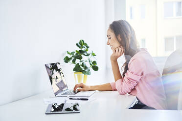 Fröhliche junge Frau arbeitet an einem Laptop im Heimbüro - BSZF01521