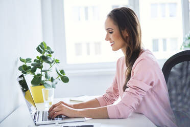 Young woman working on laptop in home office - BSZF01522