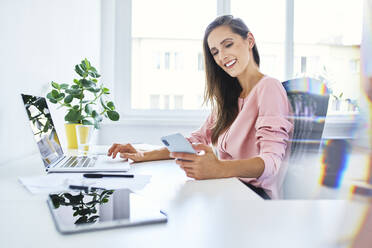 Young businesswoman checking phone while working in home office - BSZF01524