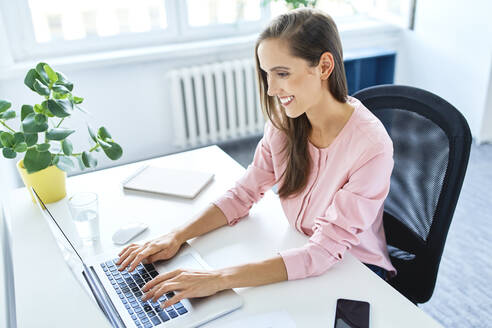 Lächelnde junge Frau, die im Büro zu Hause am Laptop arbeitet - BSZF01527