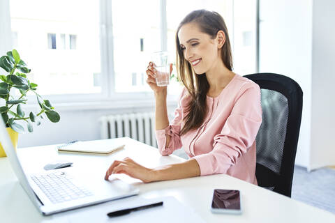 Lächelnde junge Frau, die im Büro zu Hause am Laptop arbeitet, lizenzfreies Stockfoto