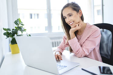 Glückliche junge Geschäftsfrau arbeitet mit Laptop im Büro - BSZF01529