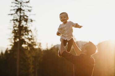 Happy father lifting up little son outdoors at sunset, Schwaegalp, Nesslau, Switzerland - LHPF01121