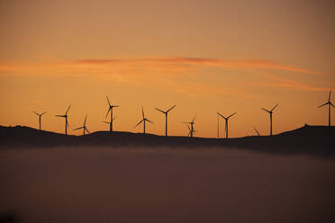Spanien, Provinz Cádiz, Tarifa, Silhouetten von Windturbinen vor stimmungsvollem Himmel bei nebligem Morgengrauen - KBF00614