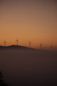 Spanien, Provinz Cádiz, Tarifa, Silhouetten von Windturbinen vor stimmungsvollem Himmel bei nebligem Morgengrauen - KBF00615