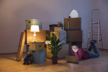 Woman using laptop surrounded by cardboard boxes in a new home - MAMF00801