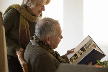 Ein älteres Ehepaar betrachtet ein Fotoalbum, das von Kartons in einem leeren Raum umgeben ist - MAMF00816