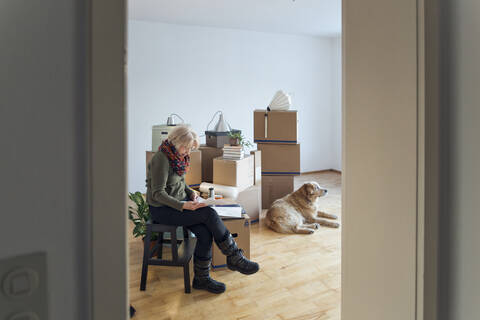 Ältere Frau schaut in einem leeren Raum auf Papiere, die von Kartons umgeben sind, lizenzfreies Stockfoto