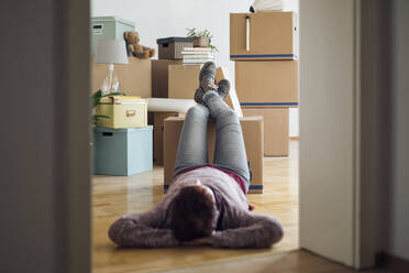 Woman relaxing surrounded by cardboard boxes in a new home - MAMF00842