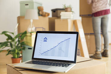 Rising line graph on laptop screen in front of cardboard boxes in a new home - MAMF00847