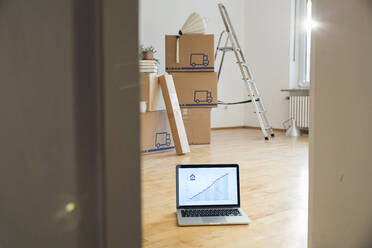 Rising line graph on laptop screen in front of cardboard boxes in an empty room in a new home - MAMF00851