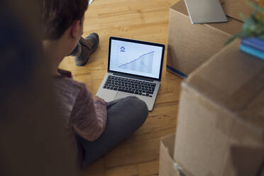 Woman using laptop with rising line graph on the screen in a new home - MAMF00855