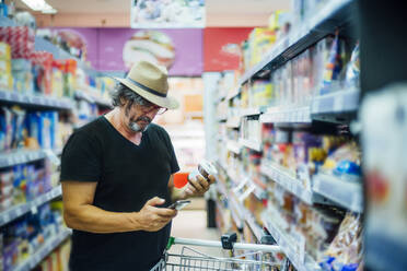 Ein älterer Mann kauft mit seinem Smartphone in einem Supermarkt ein - CJMF00117