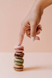 Female hand touching stack of macaroons on pink background - JMHMF00002