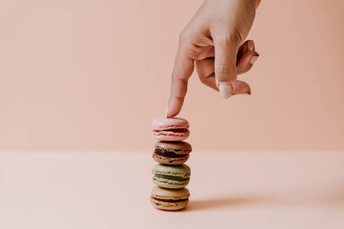 Female hand touching stack of macaroons on pink background - JMHMF00004