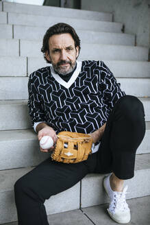 Porträt eines modischen reifen Mannes auf einer Treppe sitzend mit Baseballfänger und Ball - JLOF00342