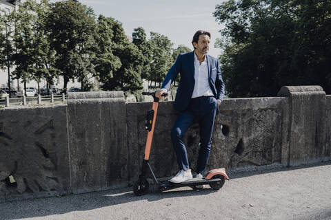 Geschäftsmann mit E-Scooter auf einer Brücke, lizenzfreies Stockfoto