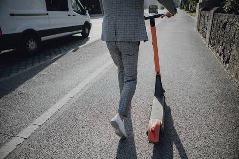 Businessman walking with e-scooter in the city - JLOF00375