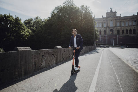 Geschäftsmann mit E-Scooter auf einer Brücke, lizenzfreies Stockfoto