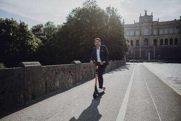 Businessman with e-scooter on a bridge - JLOF00382